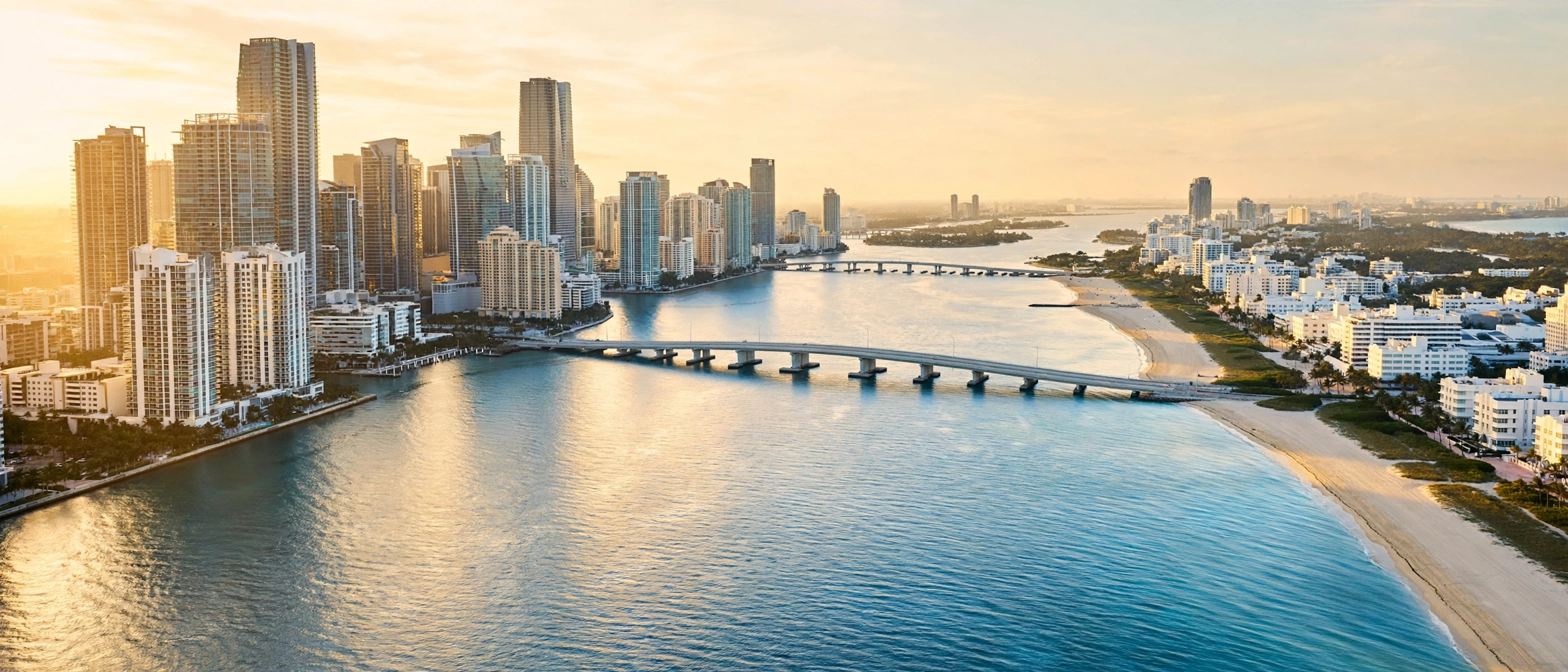 Brickell towers and Miami Beach shoreline across Biscayne Bay at golden light — moving to Miami, Brickell vs Miami Beach, cost of living in Miami, best neighborhoods in Miami